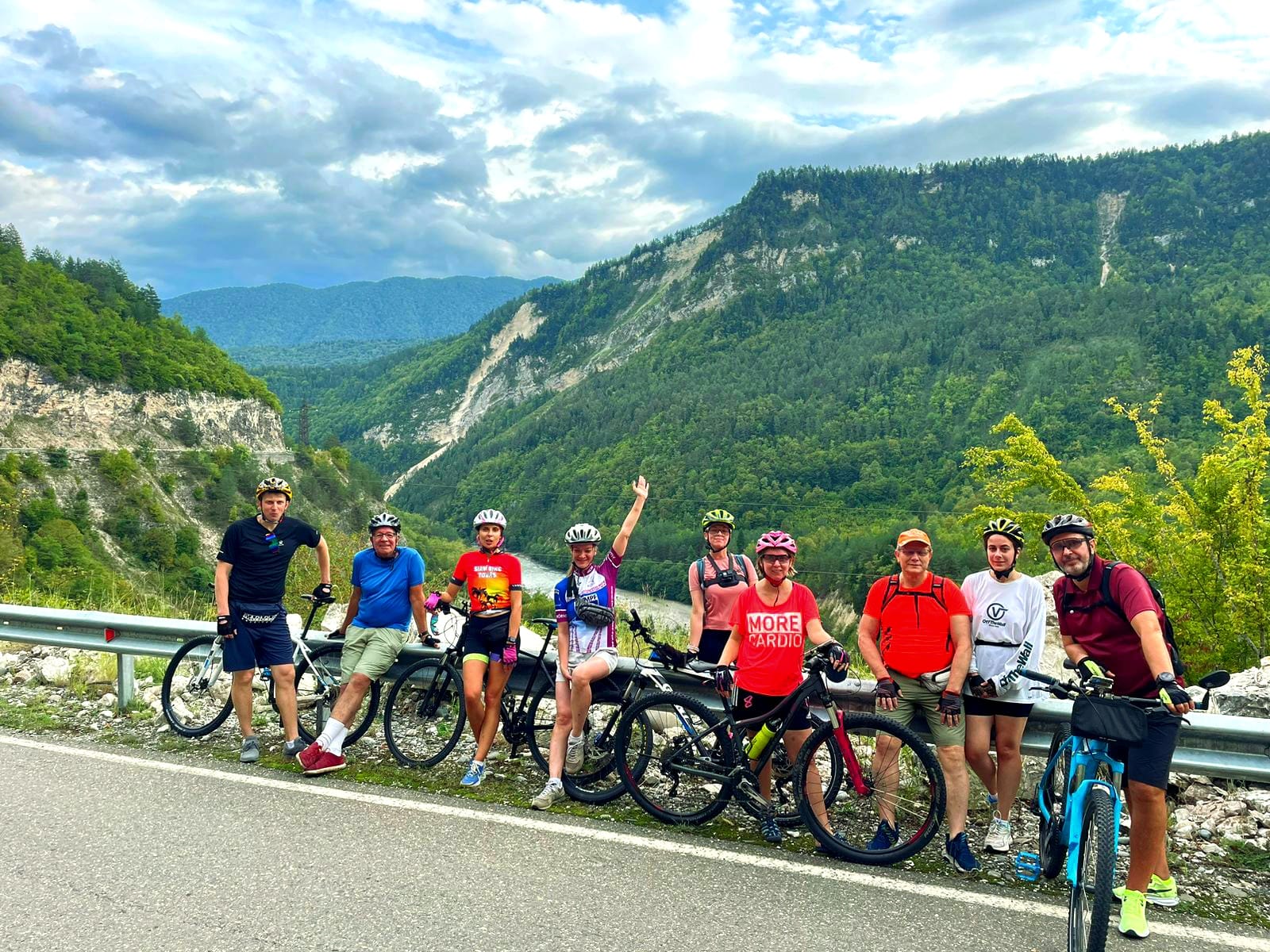 Group of smiling cyclists on a mountain road with a stunning Georgian valley behind them